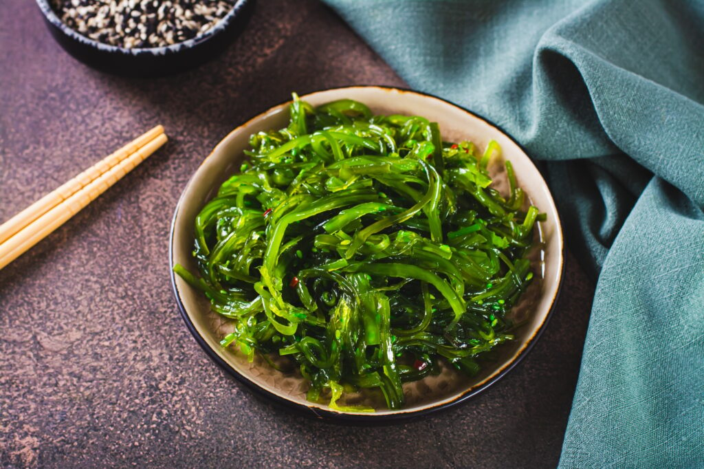 Delicious wakame seaweed salad on a plate and sesame seeds in a bowl on the table